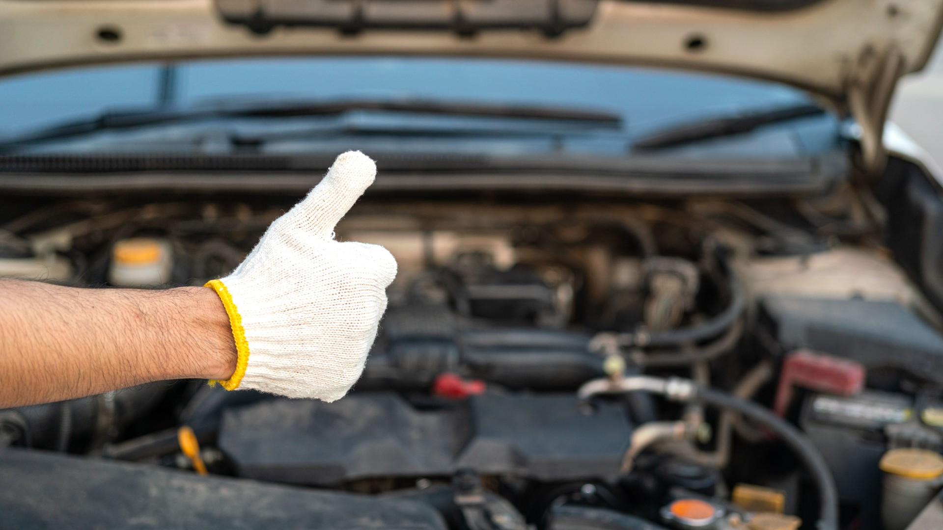 A car repairman in white cotton glove is thumbing up.